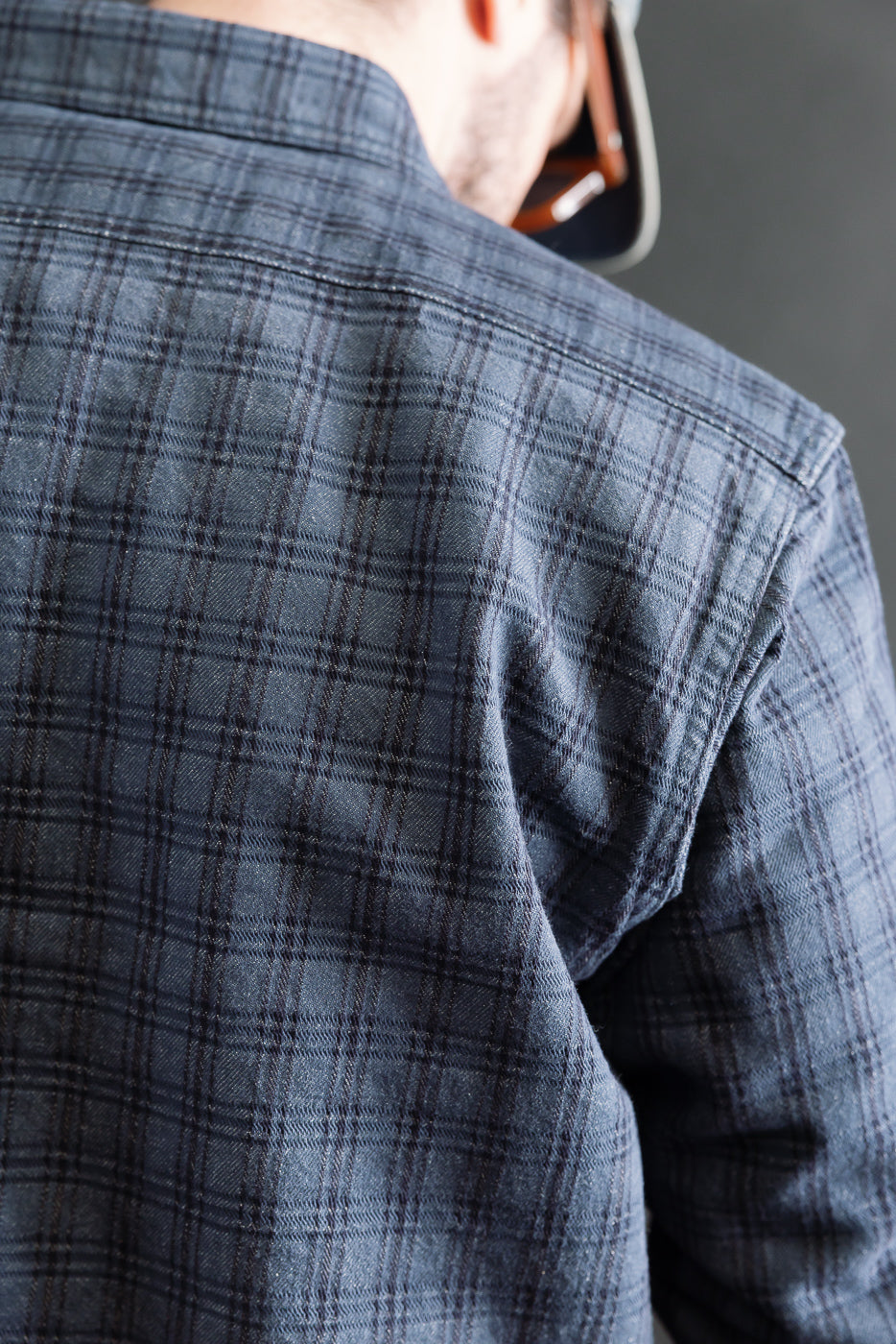 Close-up of male model's upper back in navy jacquard check work shirt, showcasing back shoulder and fabric texture. Model is 5'9