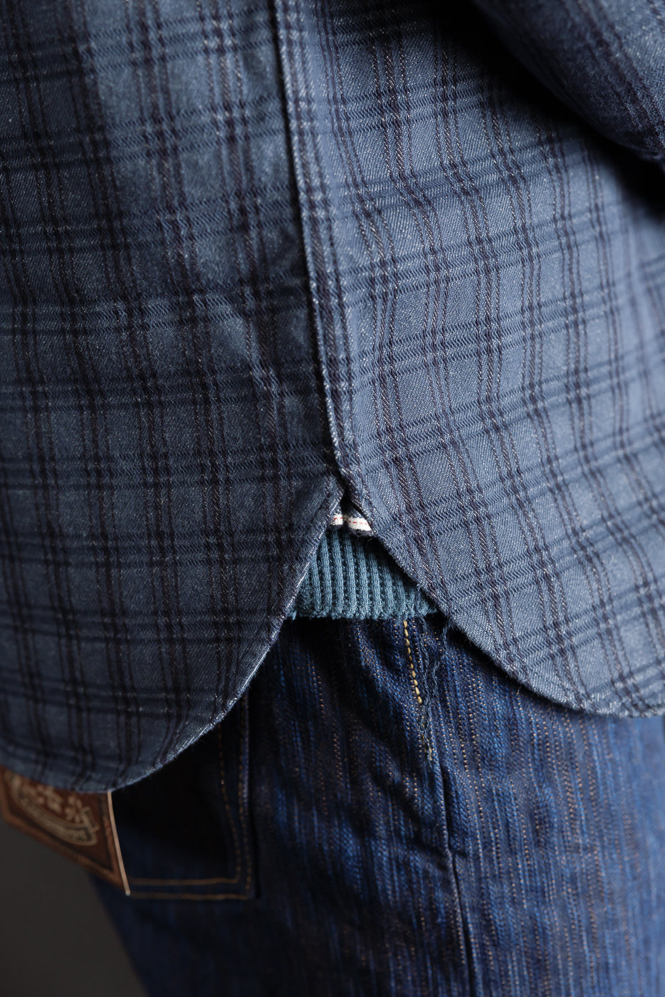 Close-up of male model wearing navy jacquard check work shirt side hem, showing fabric texture and curved hem detail.