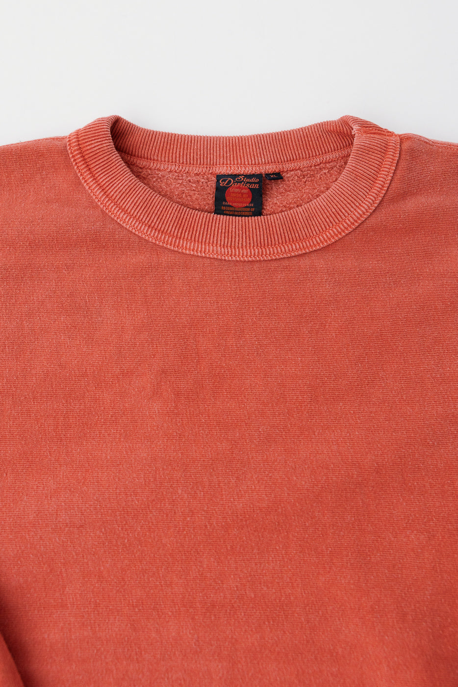 Close-up front view of Studio D'Artisan red reverse weave sweatshirt collar and tag, textured fabric.