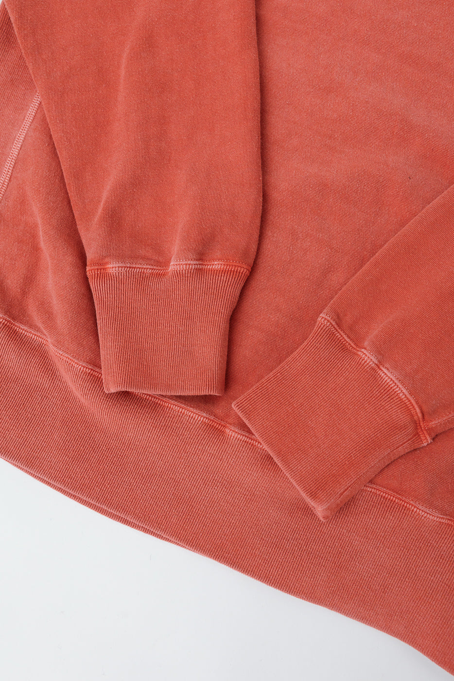 Close-up of Studio D'Artisan Bengara red sweatshirt sleeve and hem ribbing, front view, showing fabric texture and stitching detail.