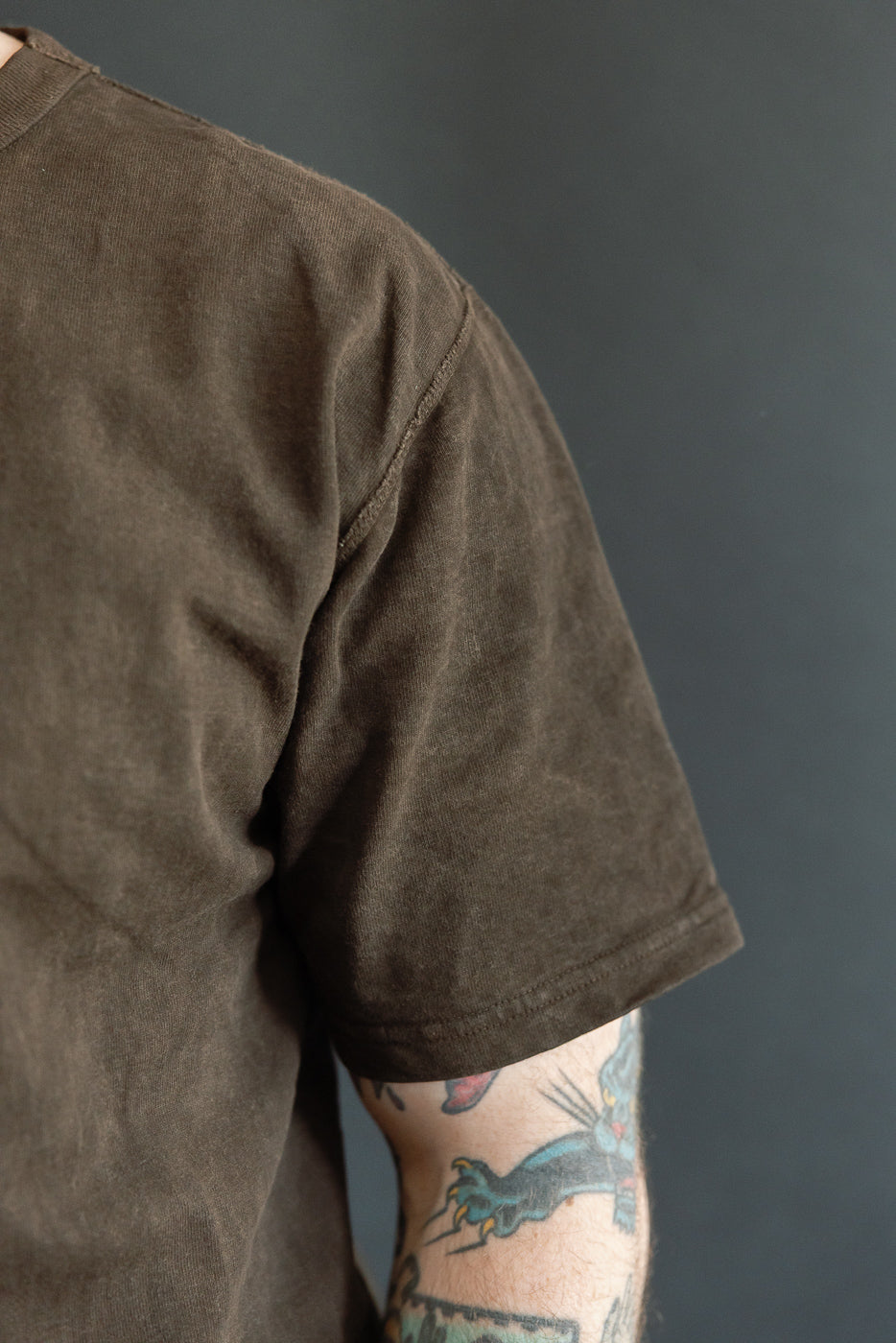 Close-up of male model's shoulder and sleeve, showcasing olive t-shirt texture and hem detail