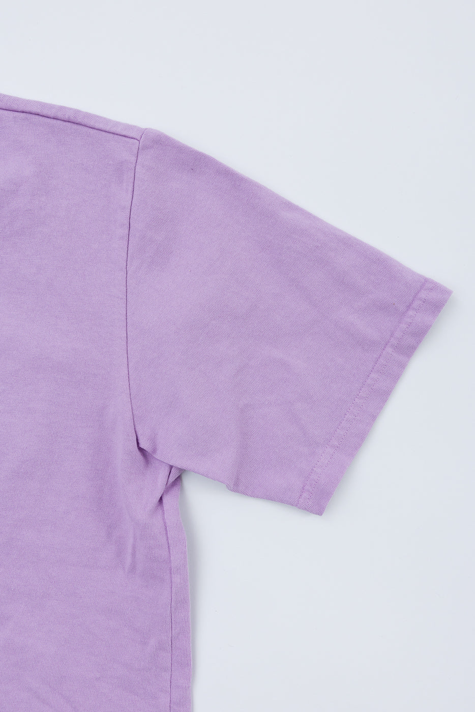 Close-up of lavender t-shirt sleeve and shoulder seam, front view, showing fabric texture and clean stitching