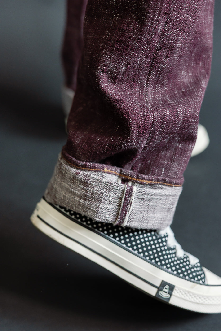 Close-up of male model's cuffed burgundy selvedge jeans with polka dot sneakers, front view