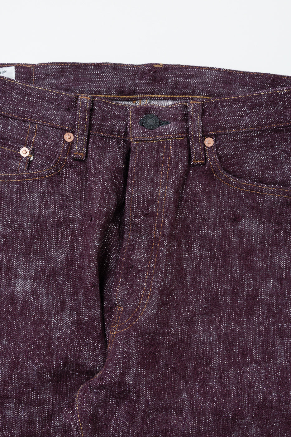 Close-up front view of dark selvedge denim jeans with copper rivets and button fly detail