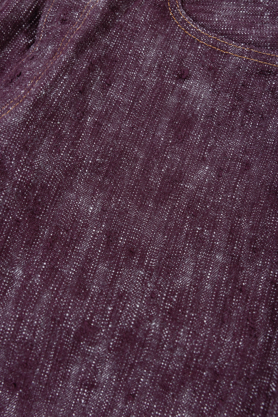 Close-up of deep purple selvedge denim fabric with white speckles and orange stitching detail
