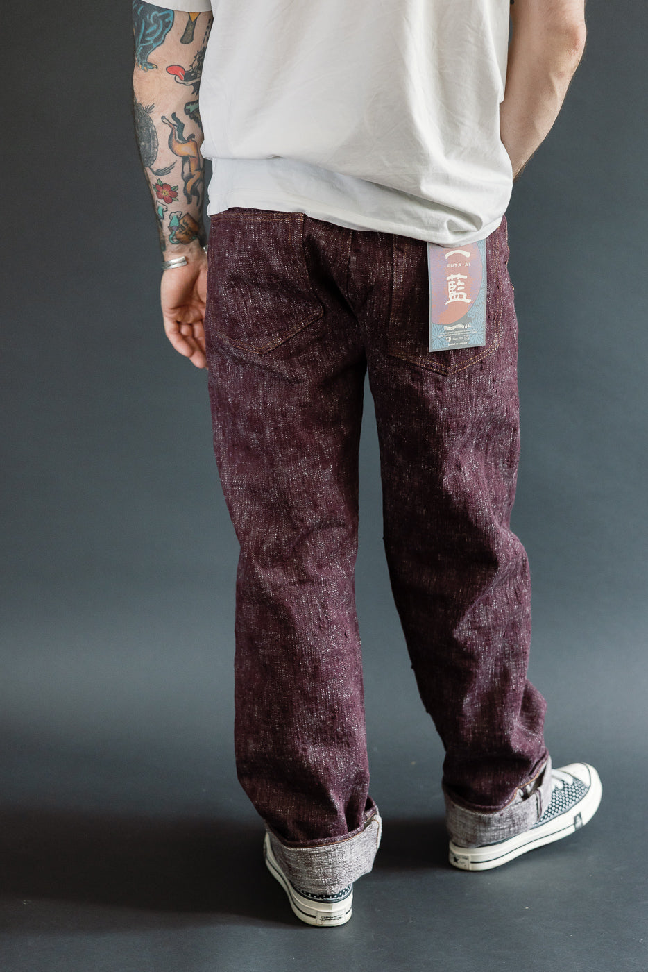 Back view of male model in dark selvedge jeans, showing tag detail and cuffed hems.