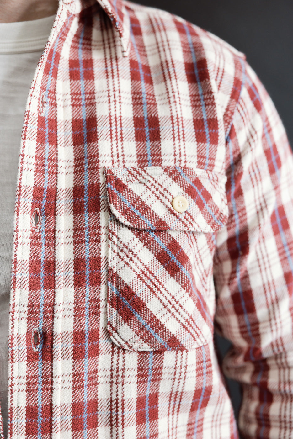 Close-up of front chest pocket and button details on maroon plaid flannel shirt, male model, athletic build