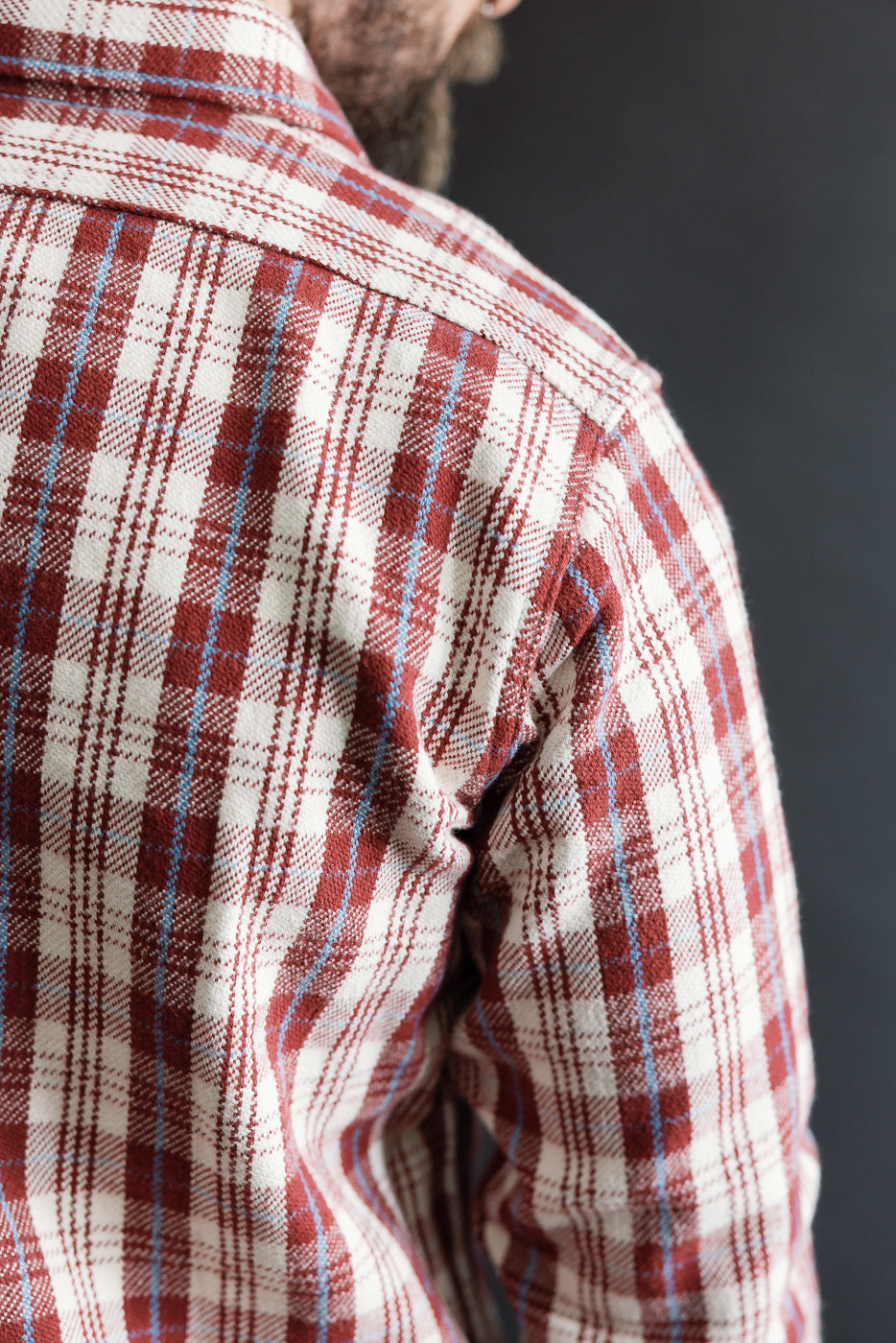 Close-up of back shoulder detail, maroon plaid flannel shirt on male model, showing fabric texture and stitching, male model is 5'9
