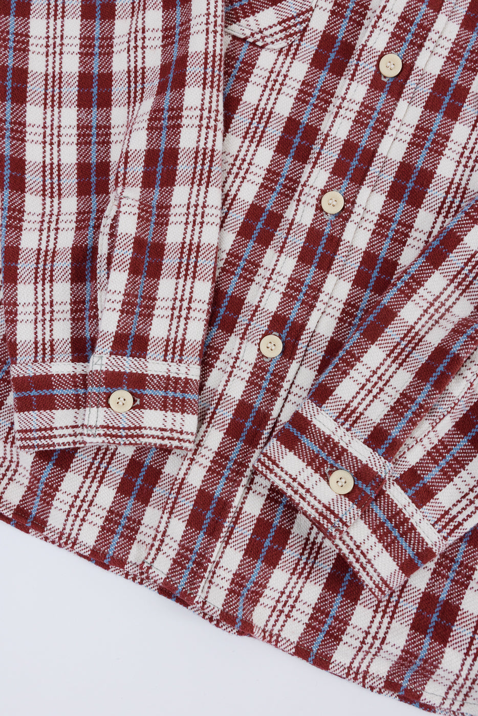 Close-up of front lower half of maroon plaid flannel shirt, showing button cuffs and soft fabric texture.