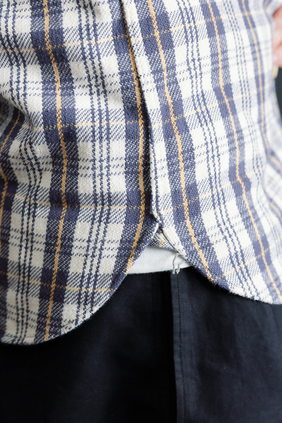 Close-up of men's flannel shirt hem, showing curved side seam, navy and cream plaid fabric texture.