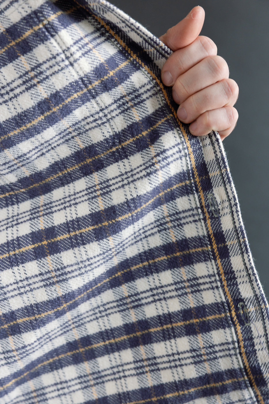 Close-up of male hand holding inside seam of navy plaid flannel shirt, fabric texture detail