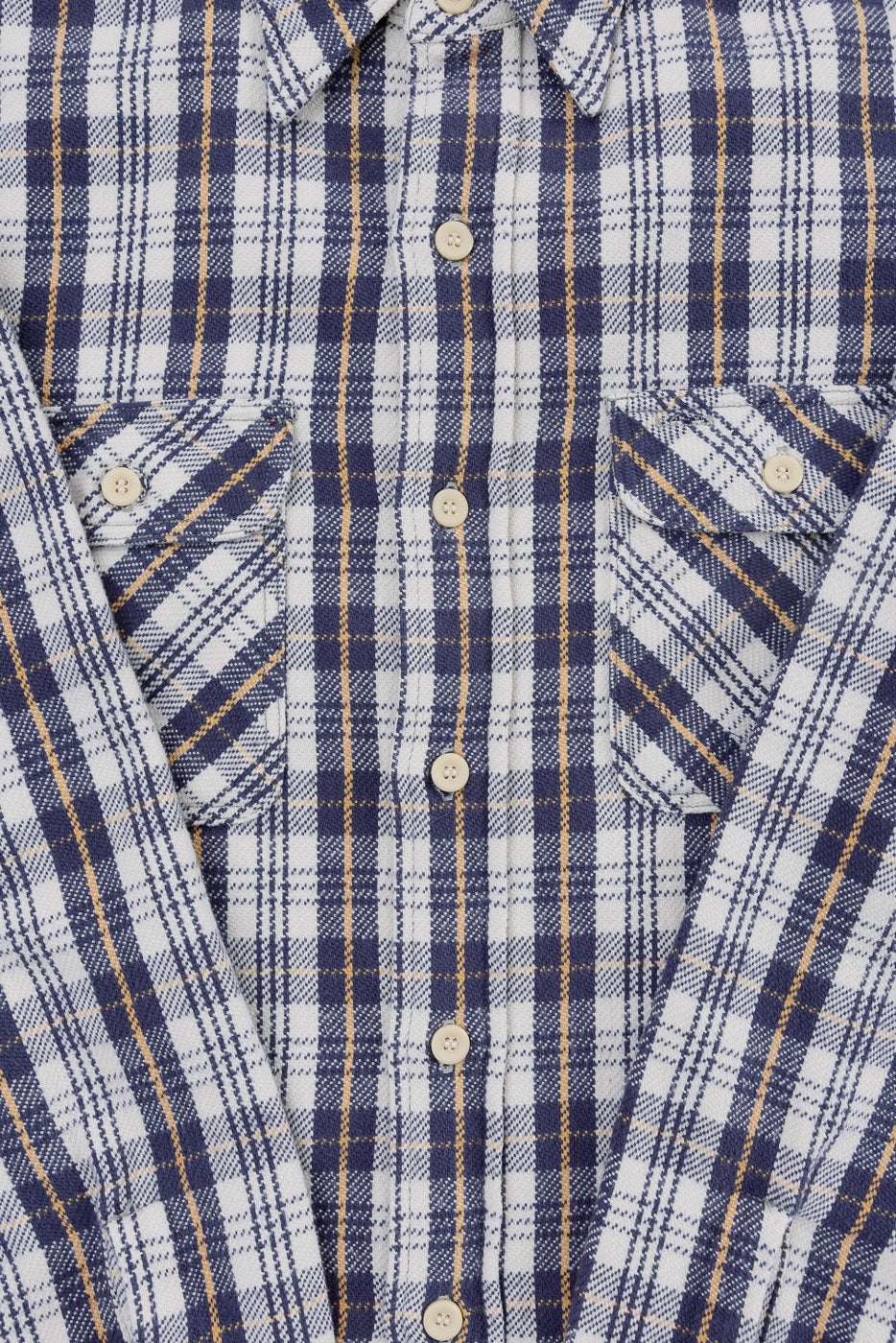Close-up of front chest and placket on navy plaid flannel shirt, showing collar, buttons, and two flap pockets.
