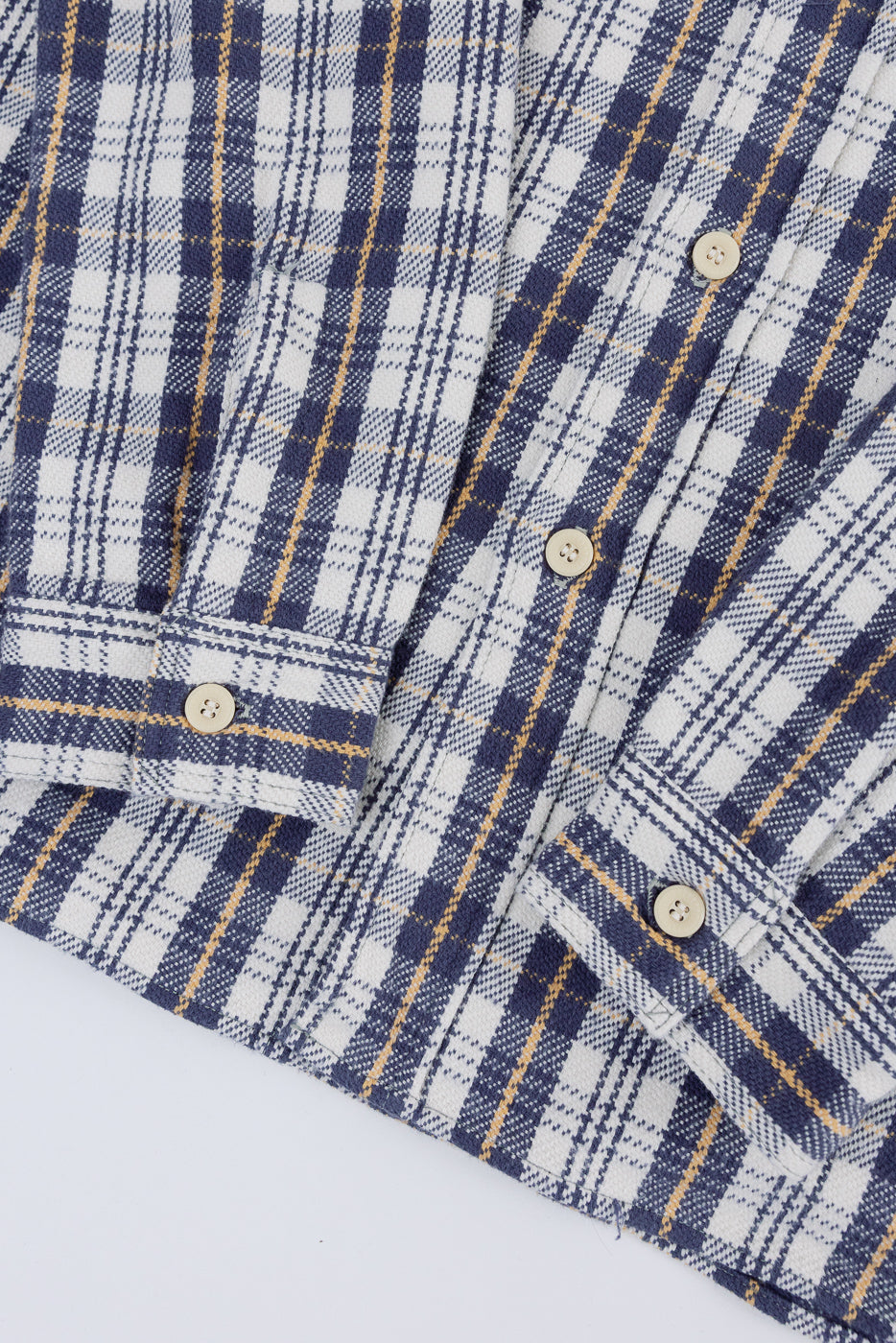Close-up of front cuffs and buttons on navy and white plaid flannel shirt, showing fabric texture.