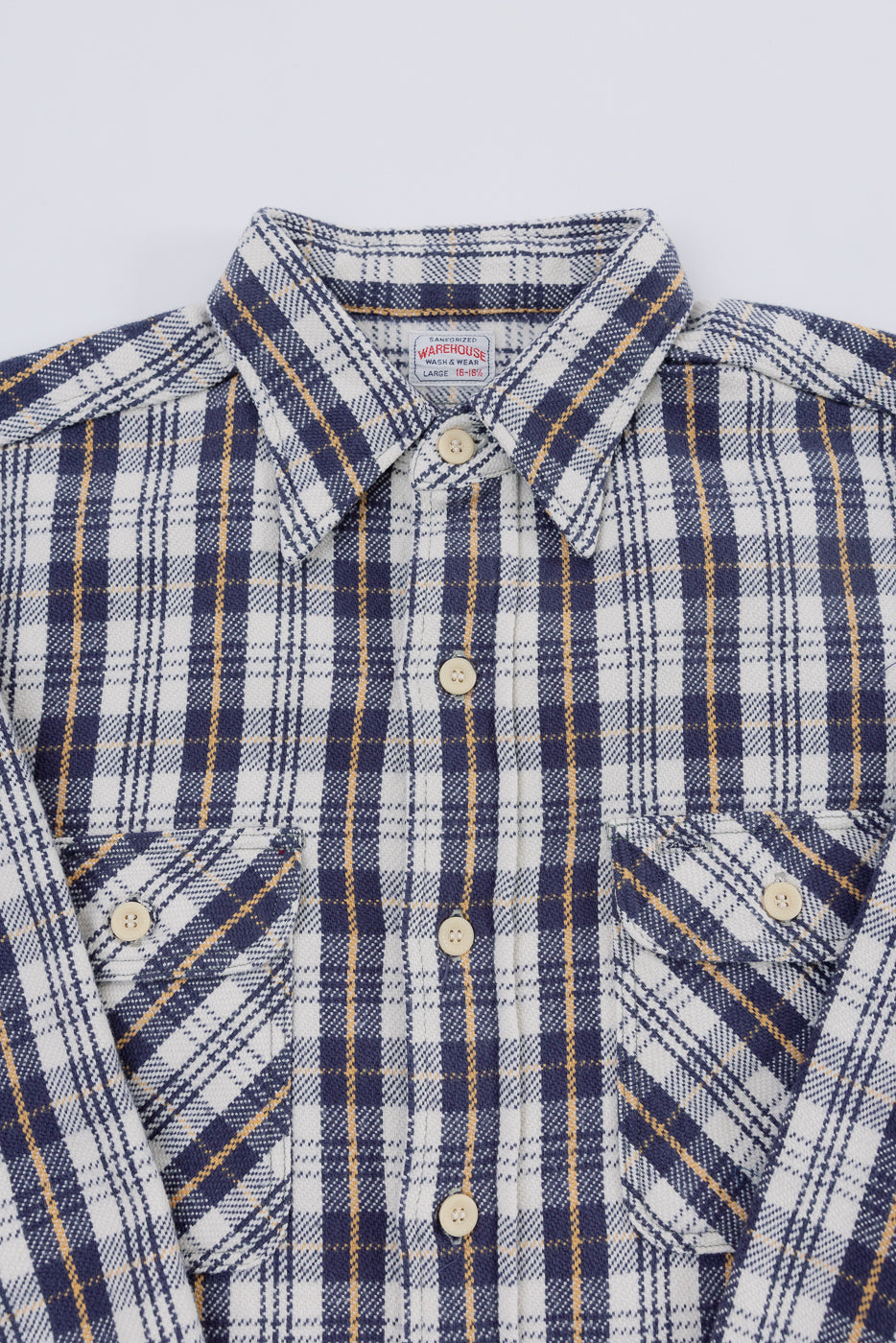 Close-up front view of navy and cream plaid flannel shirt showing collar, chest pockets, and button details.
