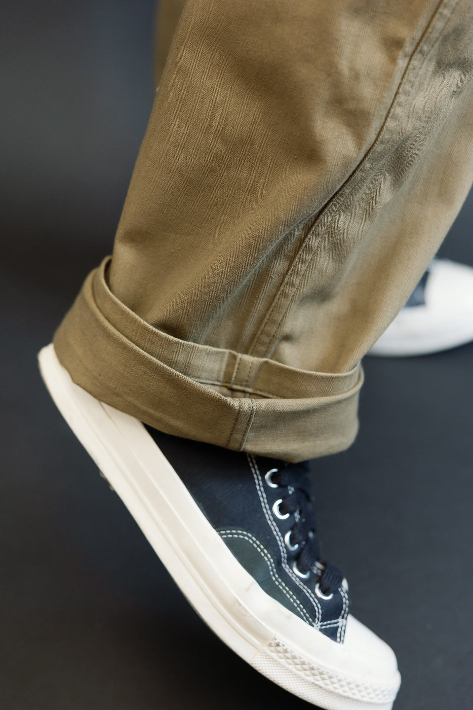 Close-up of olive cargo pants hem, cuffed over navy sneakers, showing fabric texture and stitching detail.