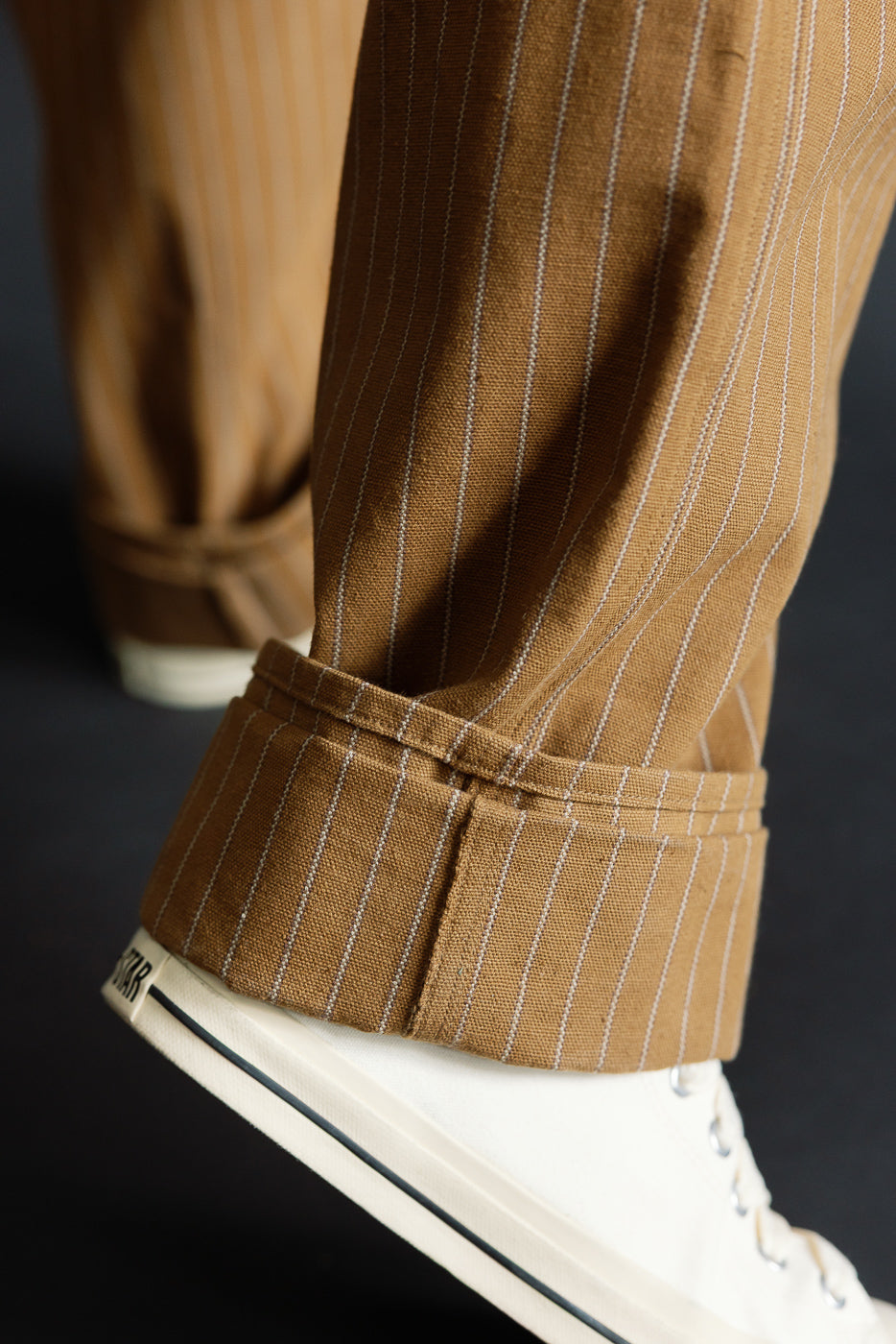 Close-up of male model's lower leg, showing front cuff detail of duck stripe trousers, pinstripe texture visible.