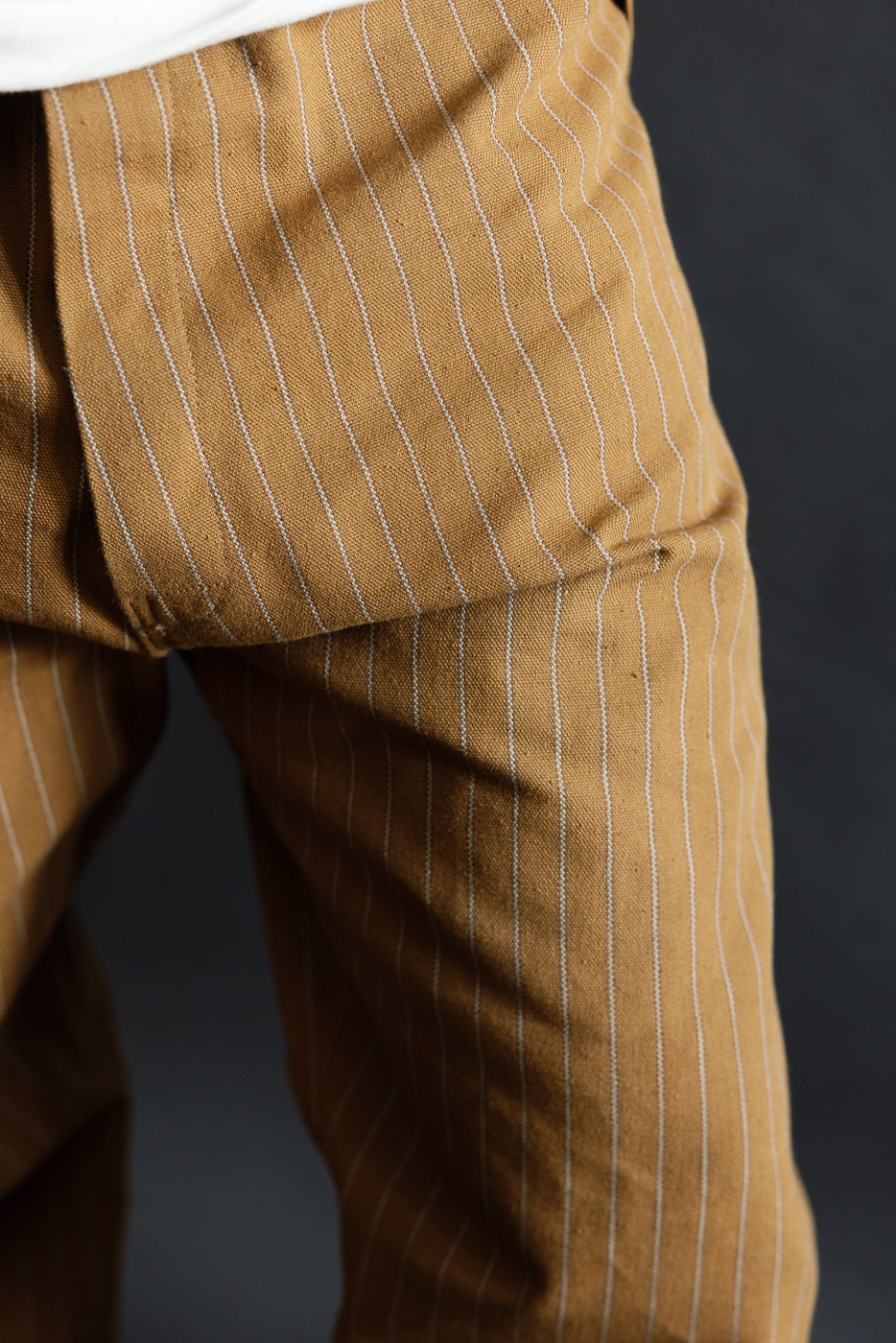 Close-up of front crotch area of brown pinstripe trousers, worn by male model, athletic build, showing fabric texture and vertical stripes.