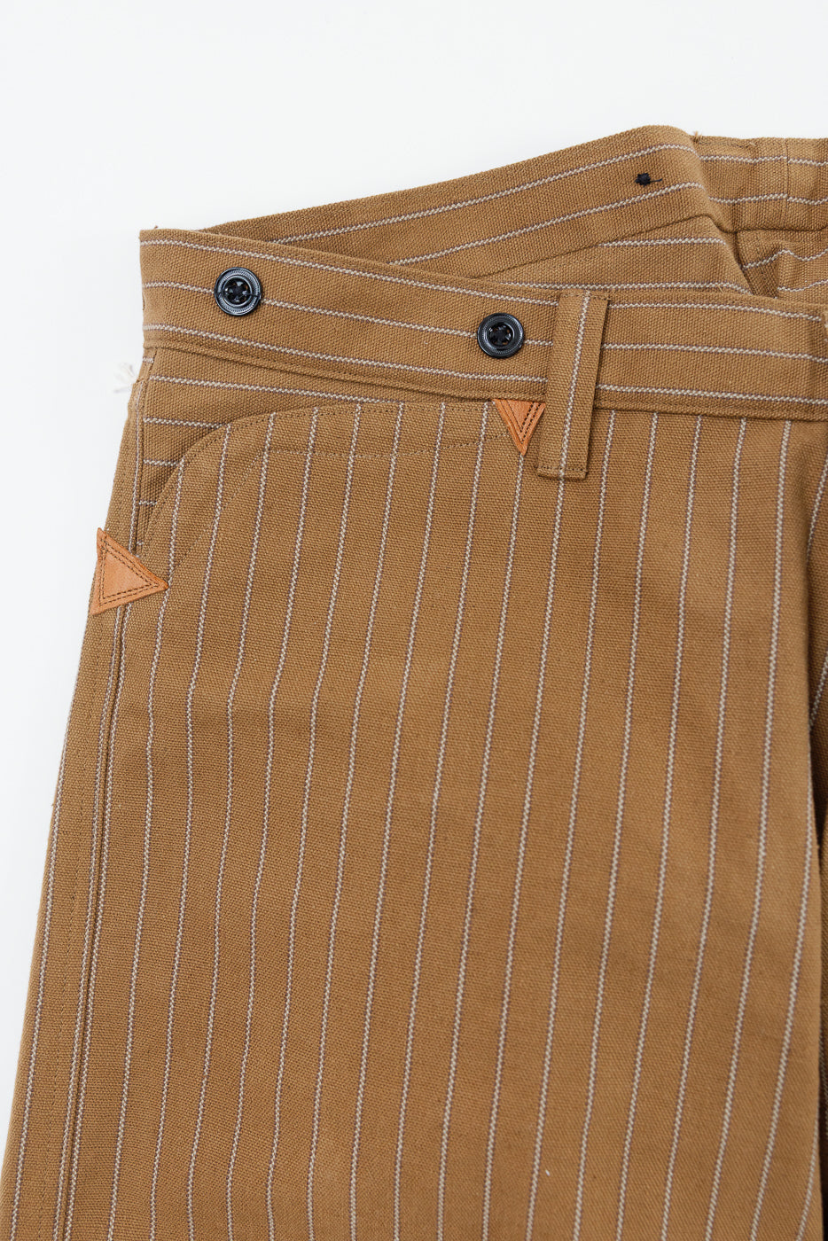 Close-up of front left hip area on brown duck stripe workwear trousers with black buttons and contrast stitching.