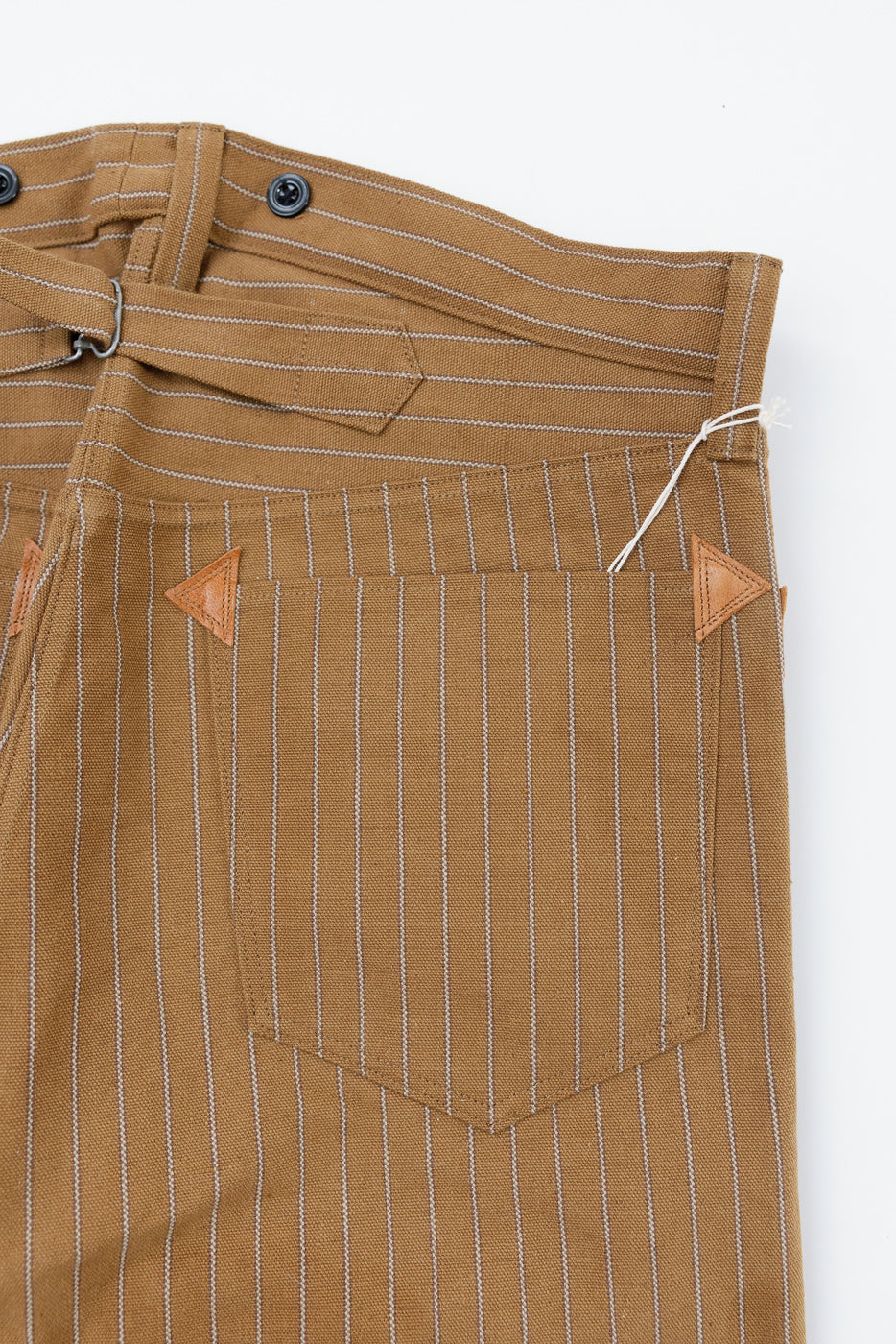 Close-up of back waist and pocket, brown duck stripe overall trousers, showing vertical pinstripes, leather reinforced pocket corners, and belt detail.