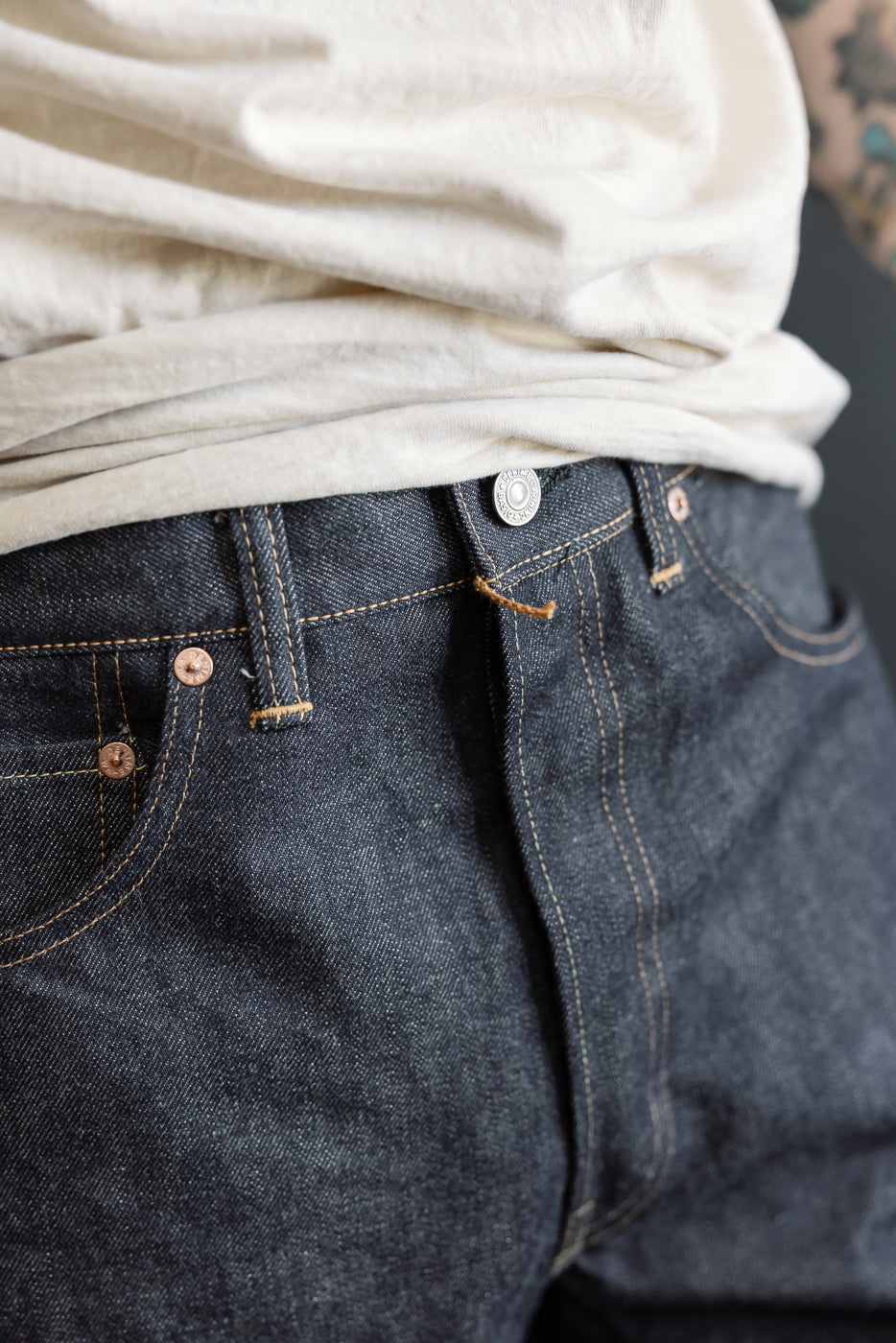 Close-up front view of indigo selvedge jeans waistband on male model, 5'9
