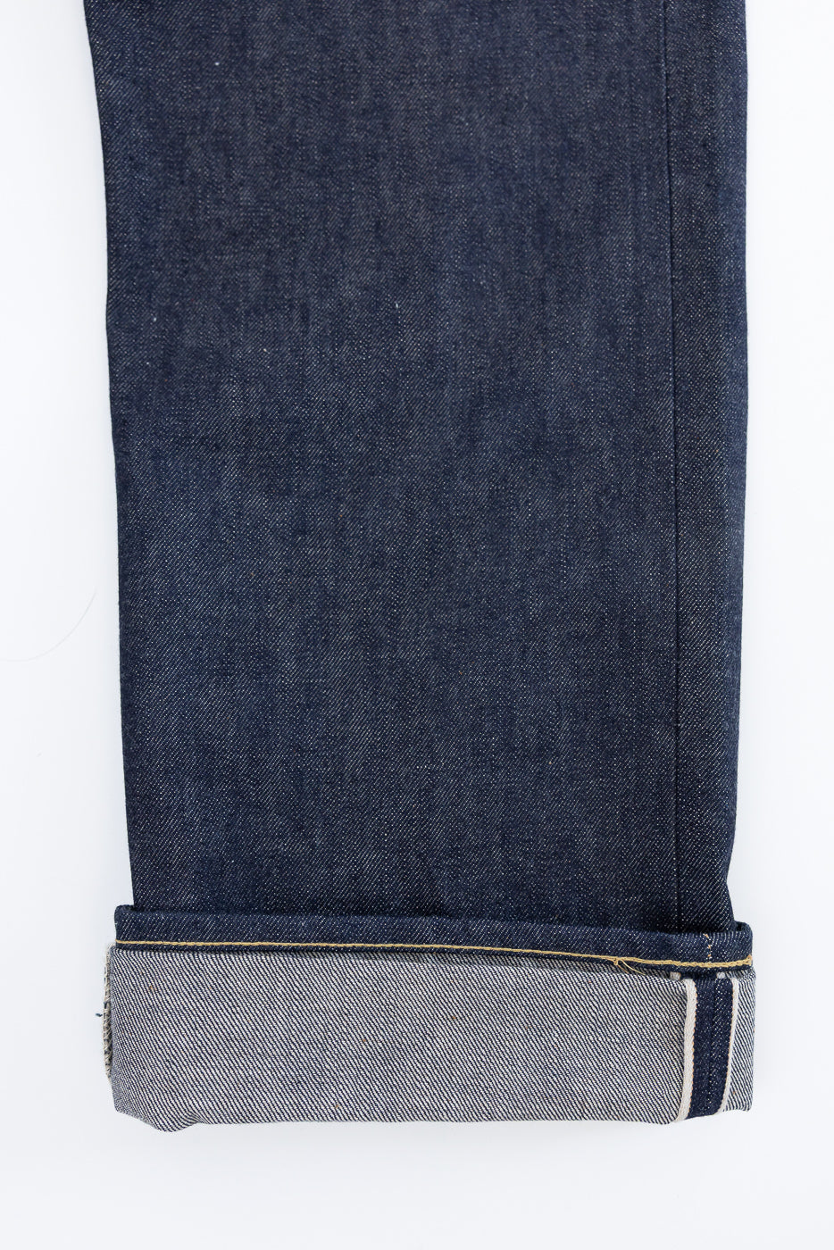 Close-up of denim jeans leg, front side, showing selvedge cuff and fabric texture.