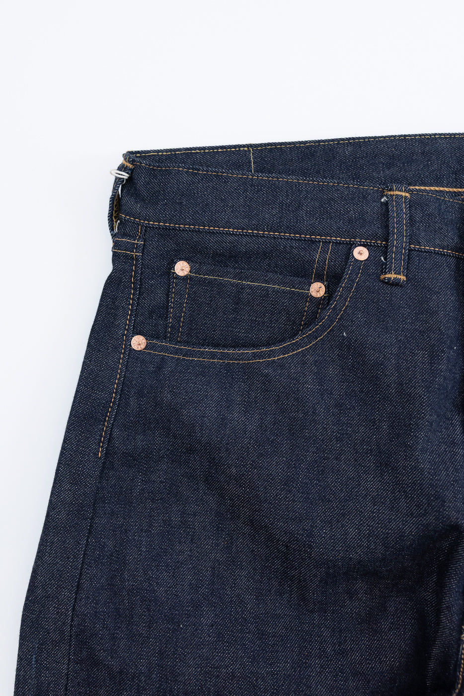 Close-up of front left hip and pocket of indigo selvedge denim jeans, showing rivets and stitching.