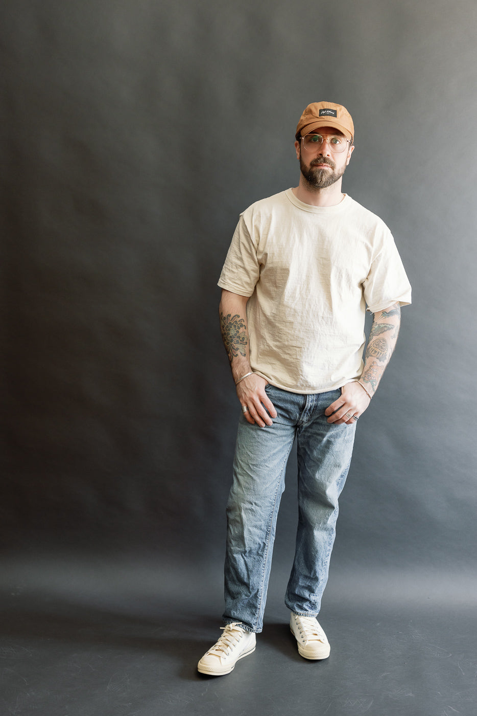 A full-length portrait of a man wearing Lot 2nd-Hand 1105 - 12oz Used Washed Indigo Denim - Tapered Fit jeans, showcasing their relaxed waist and gentle taper, styled casually with a T-shirt and sneakers.