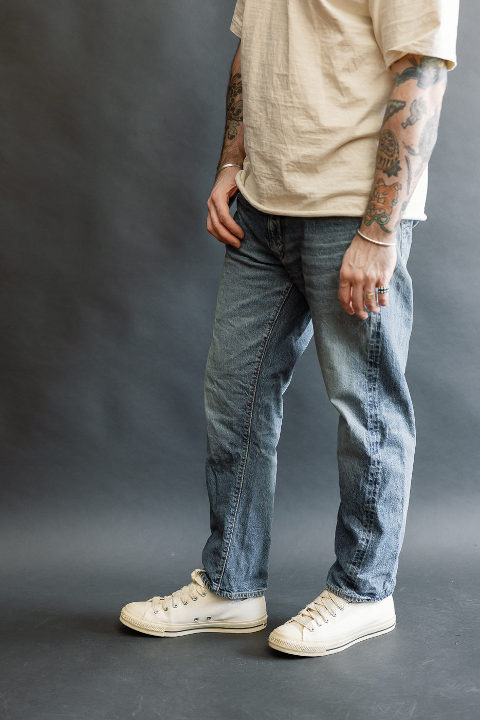 Lot 2nd-Hand 1105 - 12oz Used Washed Indigo Denim - Tapered Fit jeans, showcasing a relaxed waist and gentle taper, styled with off-white canvas sneakers and a loose tan T-shirt.