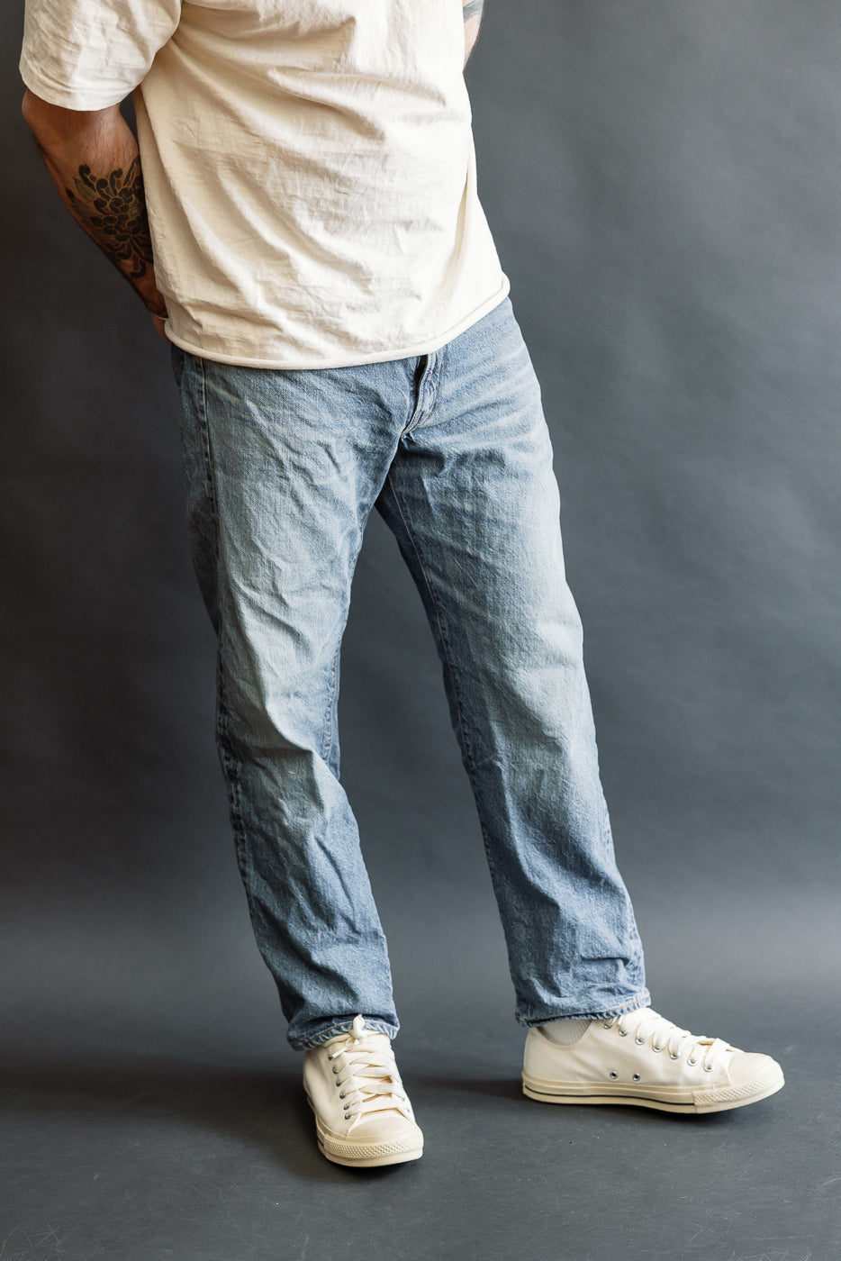 Person wearing Lot 2nd-Hand 1105 - 12oz Used Washed Indigo Denim - Tapered Fit, showcasing light-washed blue jeans with a relaxed fit and gentle taper, paired with off-white sneakers and a white T-shirt.