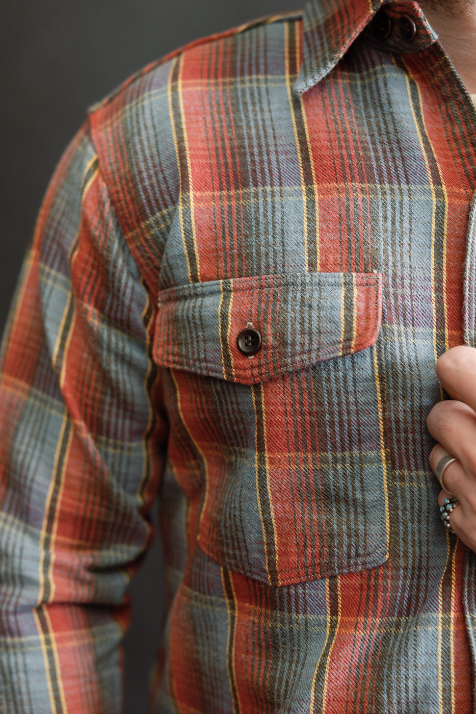 Close-up of the Lot 3022 - Flannel Shirt w/ Chinstrap G Pattern - Red, Navy, showcasing the plaid design, chest pocket with a dark button, and the wearer's ring-adorned hand resting near the shirt front.