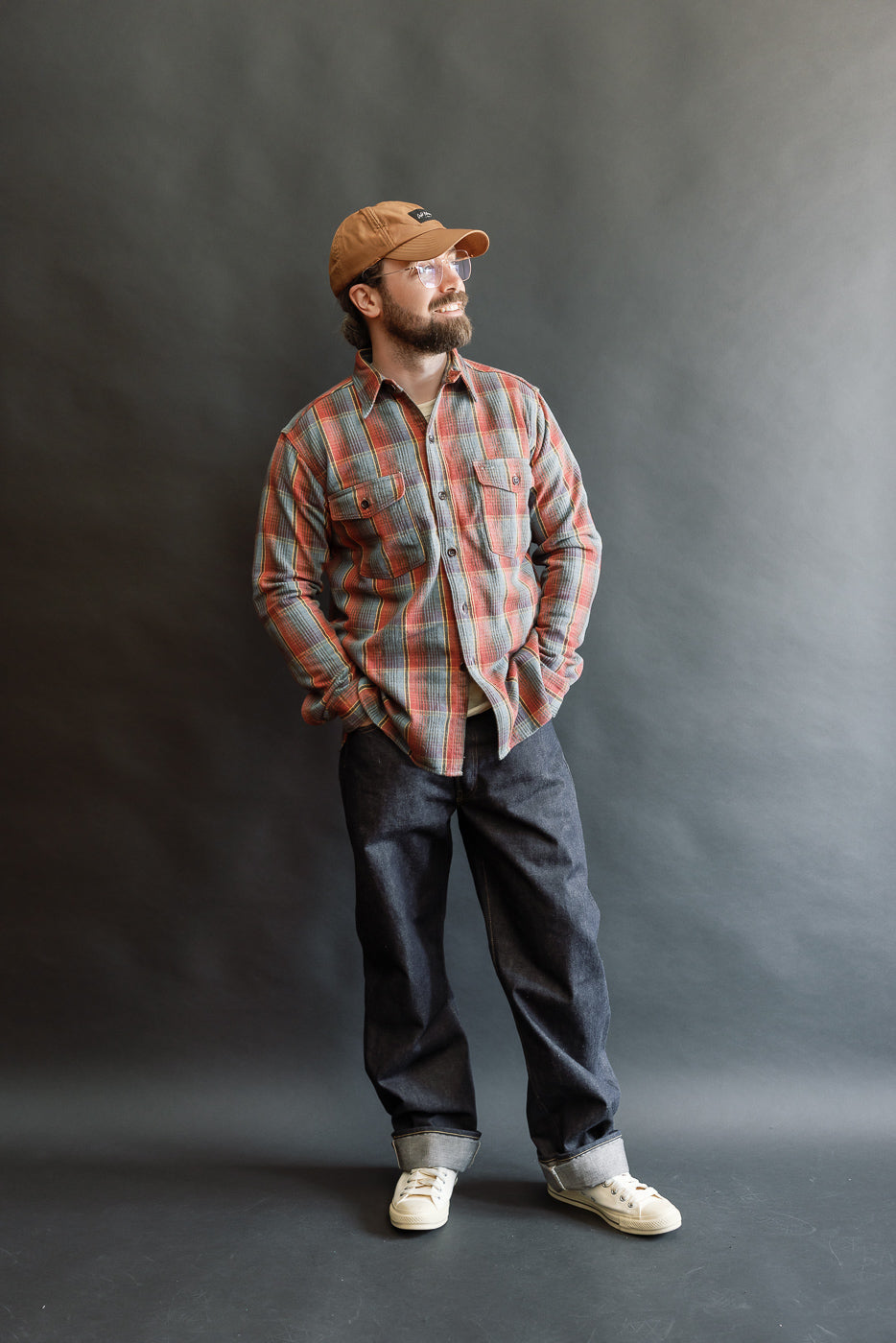 Man models Lot 3022 Flannel Shirt with Chinstrap, showcasing its G Pattern design and vintage-inspired details, paired with dark denim jeans and off-white canvas sneakers against a plain backdrop.