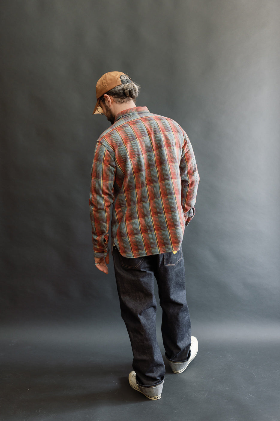 Man models the Lot 3022 - Flannel Shirt w/ Chinstrap G Pattern - Red, Navy, showcasing its vintage-inspired design with rolled cuffs, complemented by dark jeans and white sneakers.