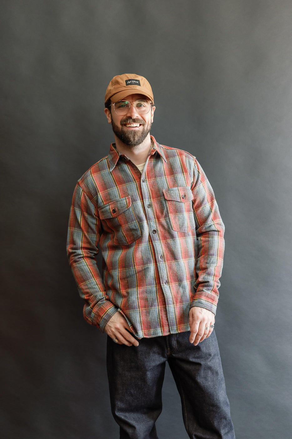Man models Lot 3022 Flannel Shirt w/ Chinstrap G Pattern. The plaid shirt features vintage-style details, paired with dark denim jeans, showcasing Dant's heritage-inspired menswear.