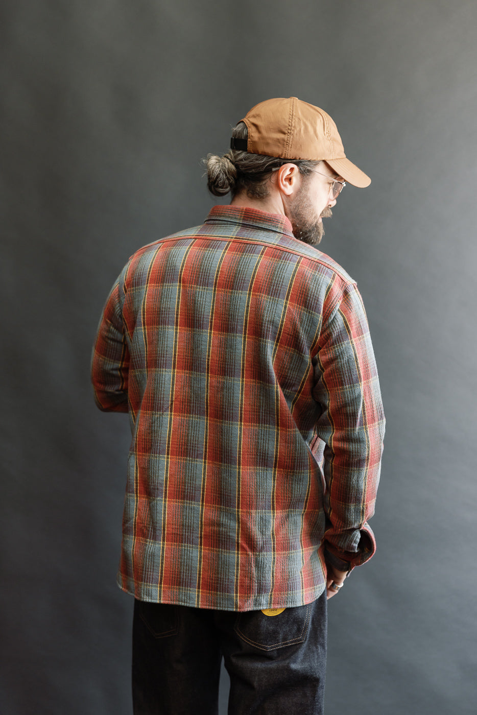 Man wearing the Lot 3022 Flannel Shirt w/ Chinstrap G Pattern - Red, Navy, styled with a brown cap and glasses, showcasing its classic plaid design and vintage-inspired workwear details against a neutral background.