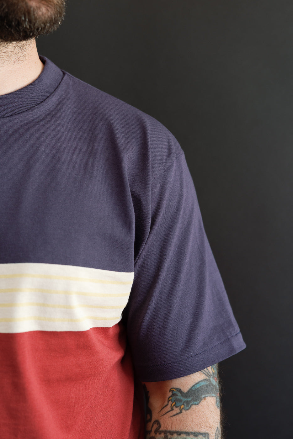Close-up side view of a color-block t-shirt on a male model, showing purple, cream, and red fabric.