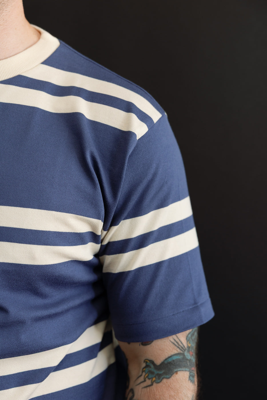 Close-up side view of male model in navy & cream striped tee, showing sleeve hem and ribbed collar, athletic build