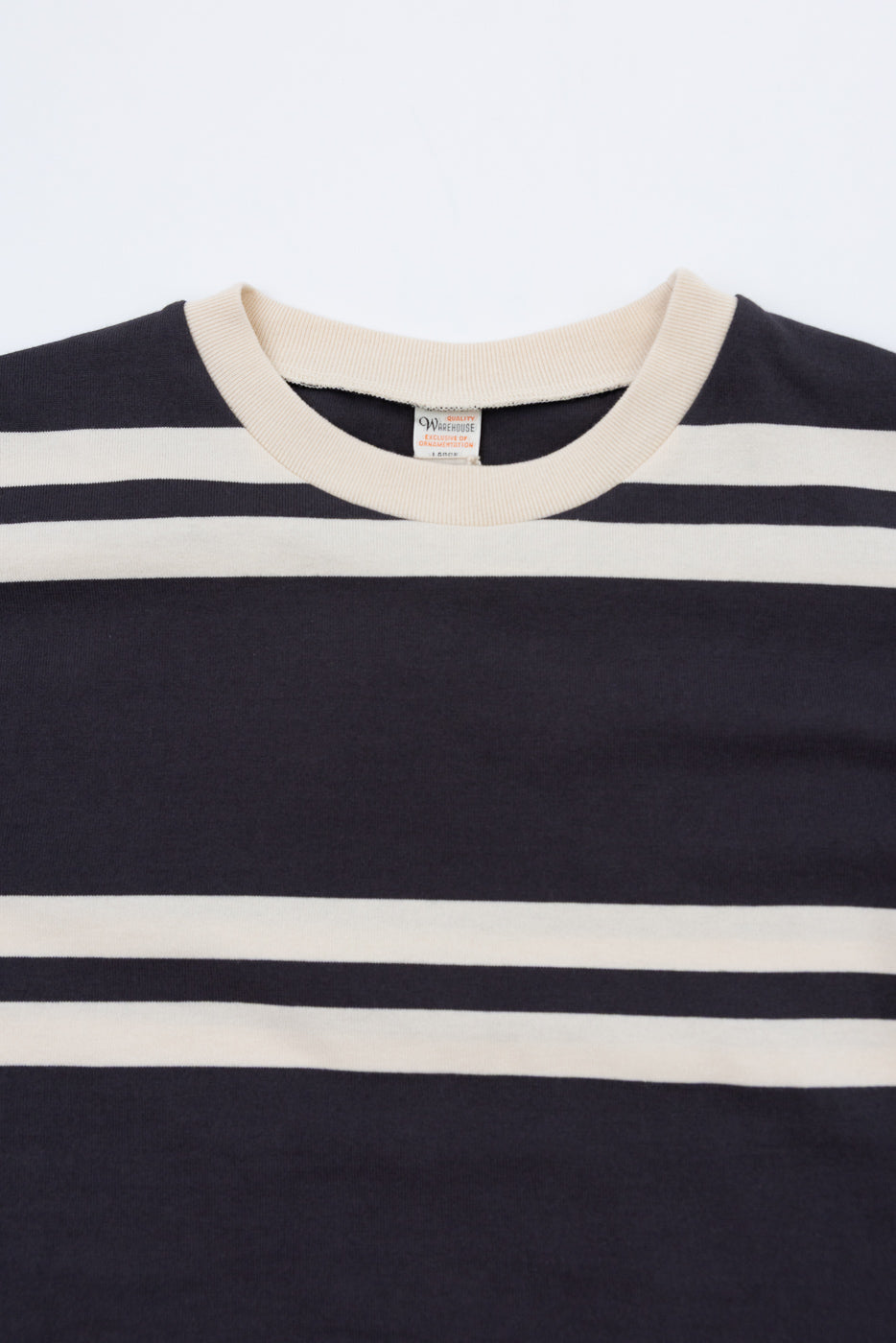Close-up front view of striped crewneck tee, cream collar, tag visible, navy and cream horizontal stripes