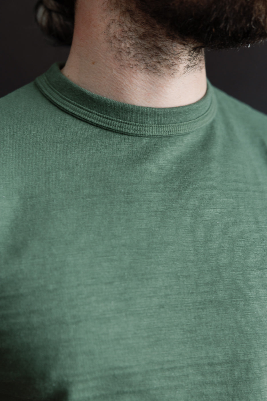 Close-up of front chest and collar detail on green slubby cotton T-shirt, crew neck, male model, athletic build, 5'9