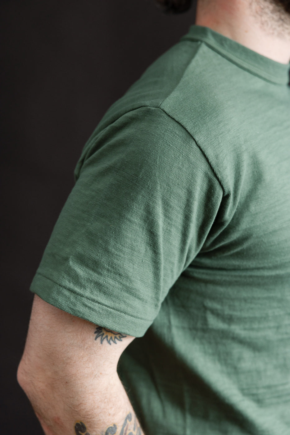 Close-up of male model's right side wearing green slubby cotton T-shirt, sleeve detail visible, model is 5'9