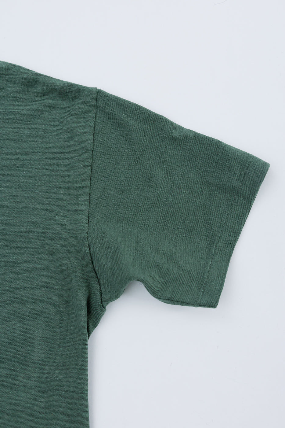 Close-up of green slubby cotton t-shirt, showing right sleeve and side seam detail, flat lay view.