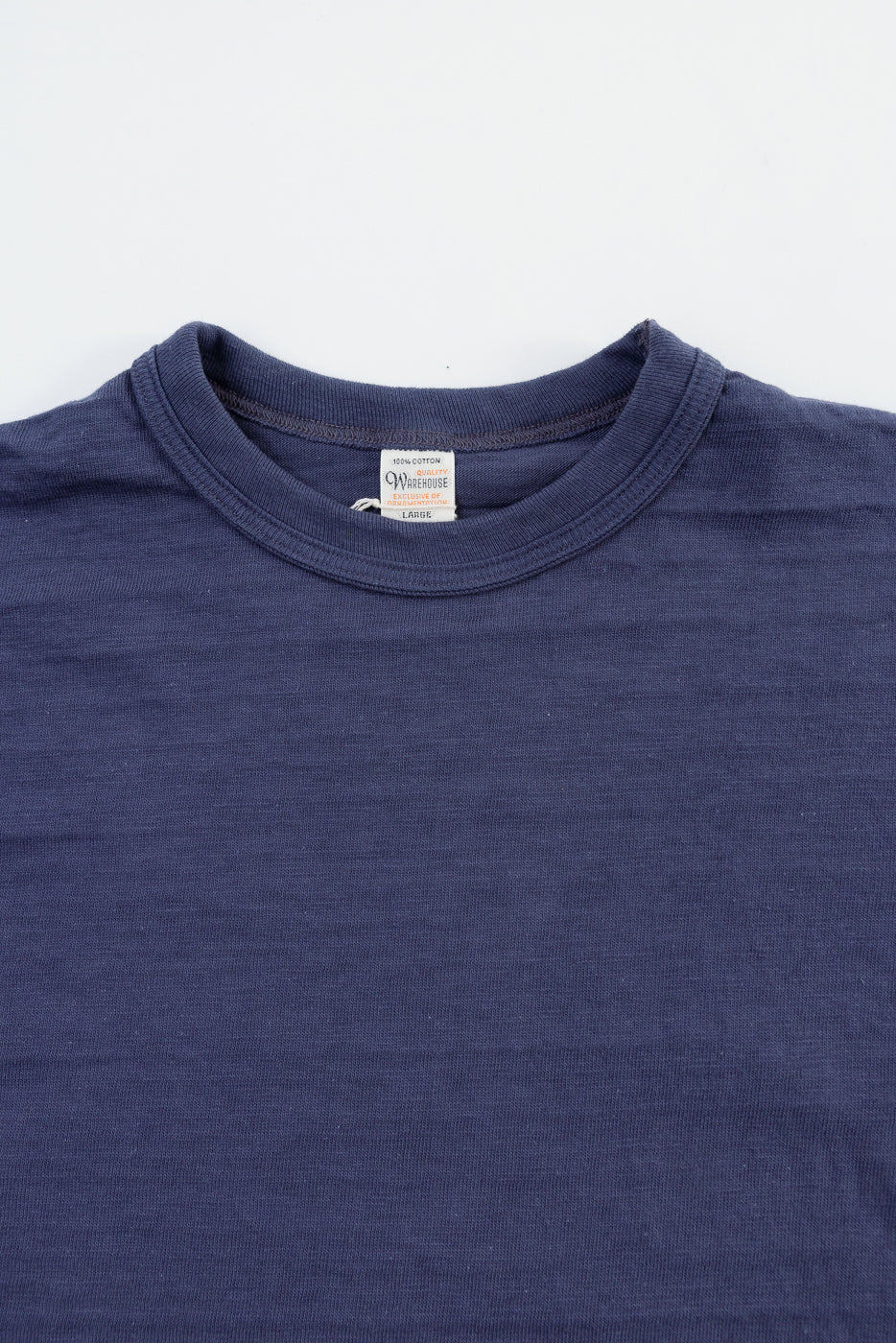 Close-up of front upper chest and collar of heather eggplant slubby cotton t-shirt, fabric texture and tag detail visible.
