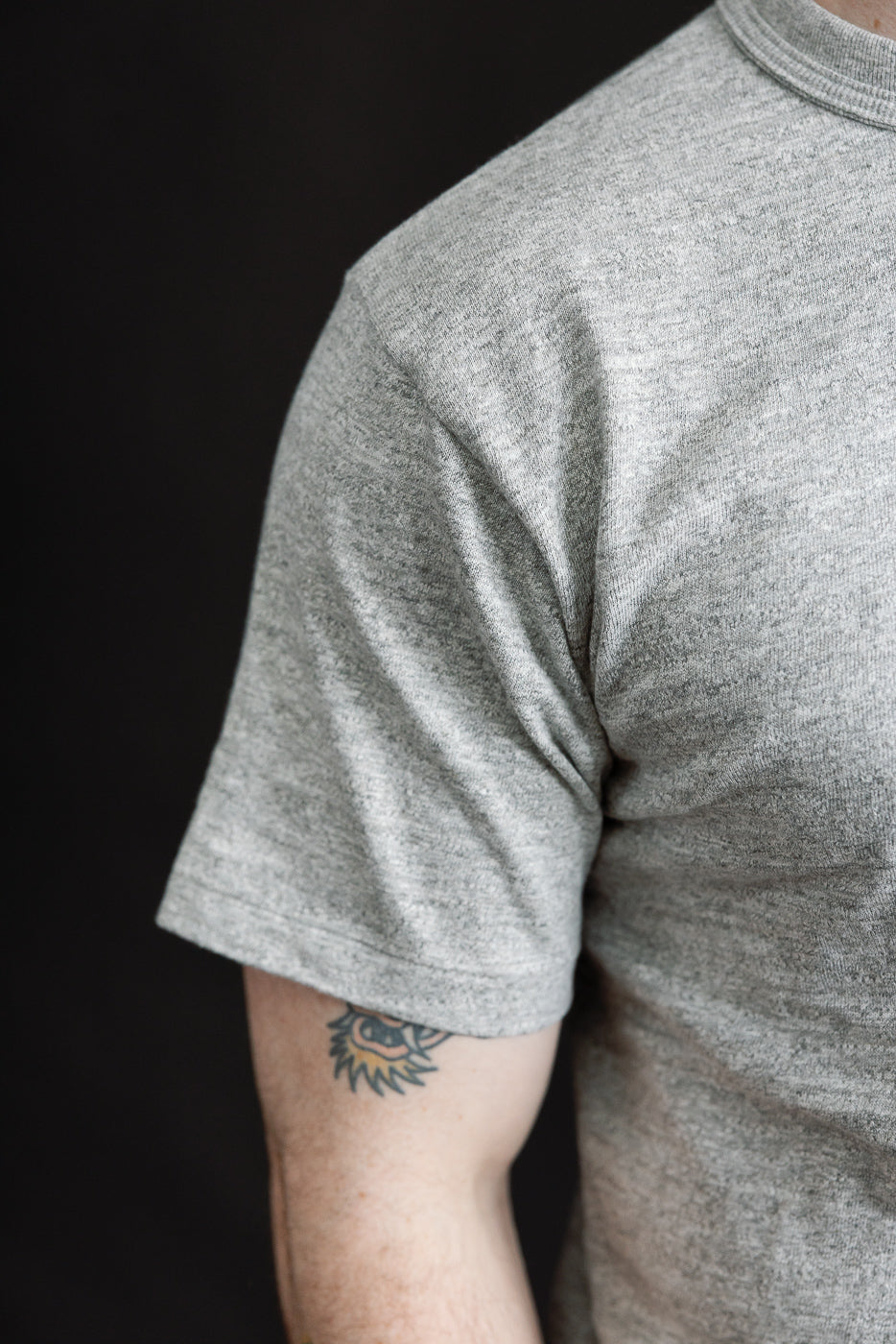 Close-up of male model's right side wearing heather grey slubby cotton t-shirt, sleeve and fabric texture visible, model is 5'9