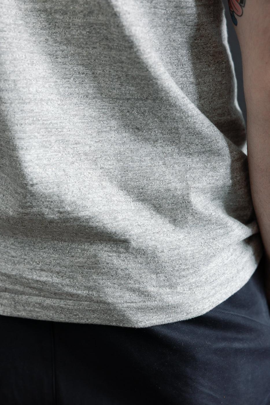 Close-up of heather grey slubby cotton t-shirt side hem on male model, highlighting fabric texture
