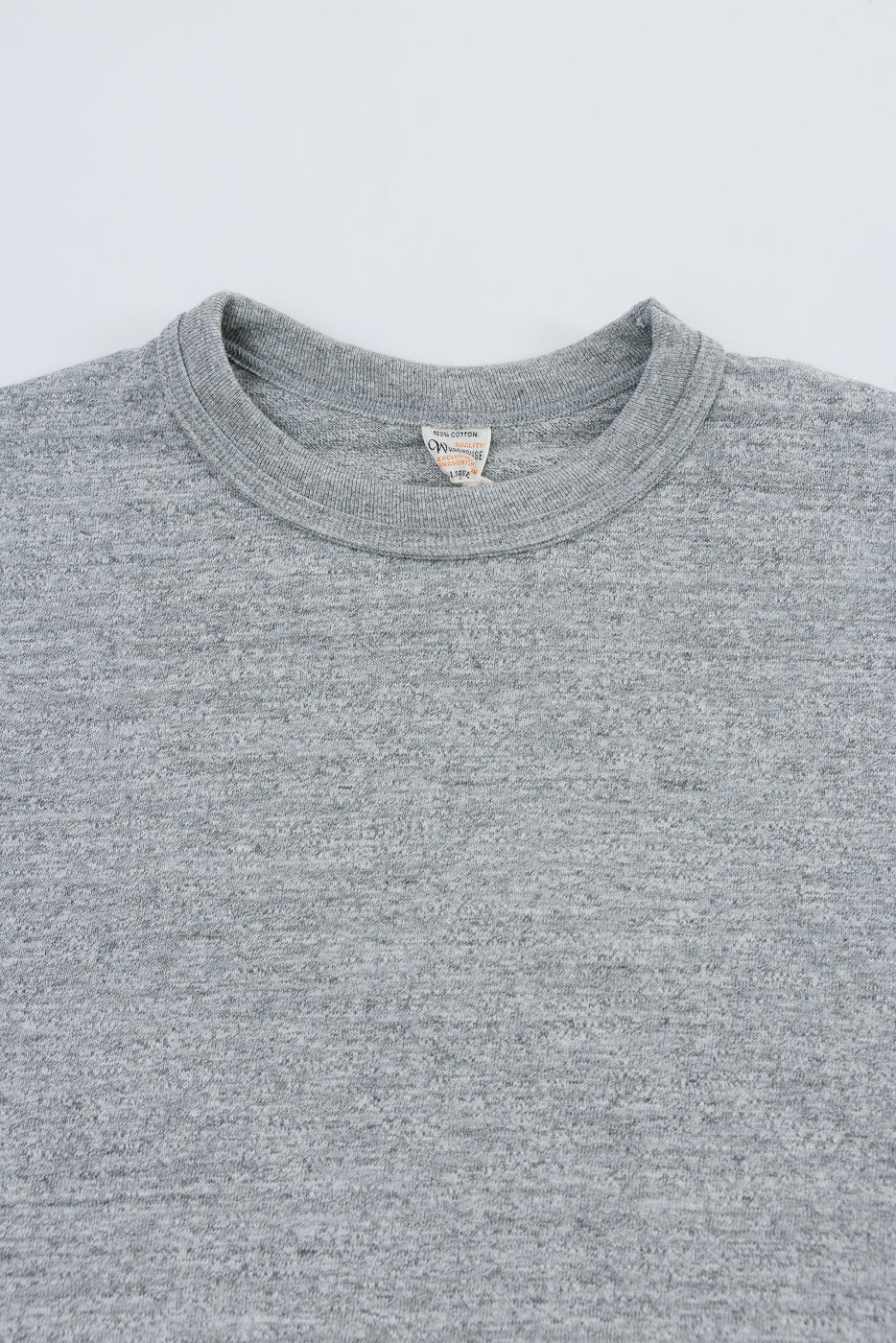 Close-up of front upper chest and collar on heather grey slubby cotton t-shirt, showing textured fabric and tag detail.