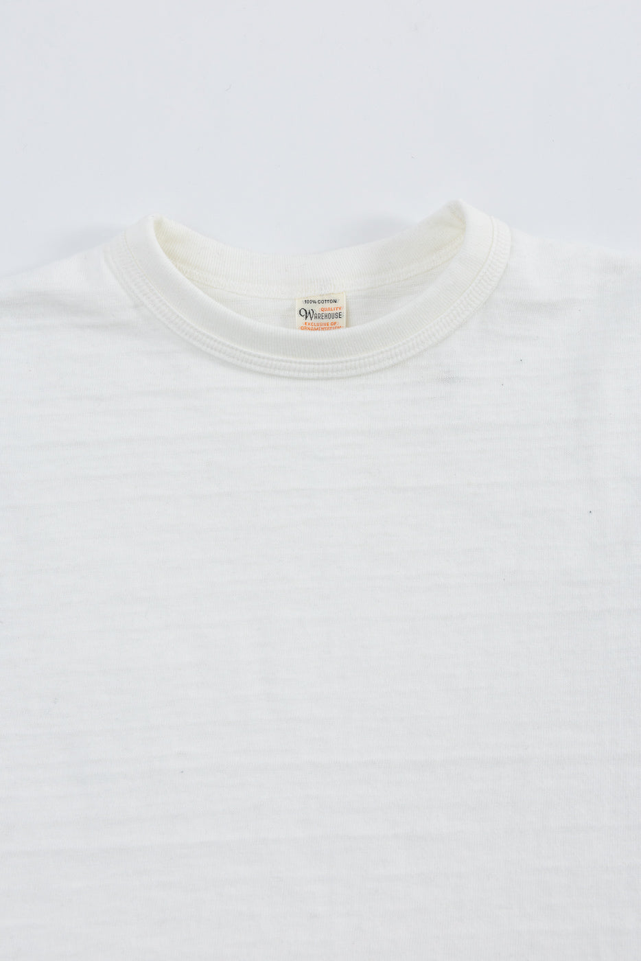 Close-up of front upper chest and collar of off-white slubby cotton t-shirt, neckline and tag detail shown.
