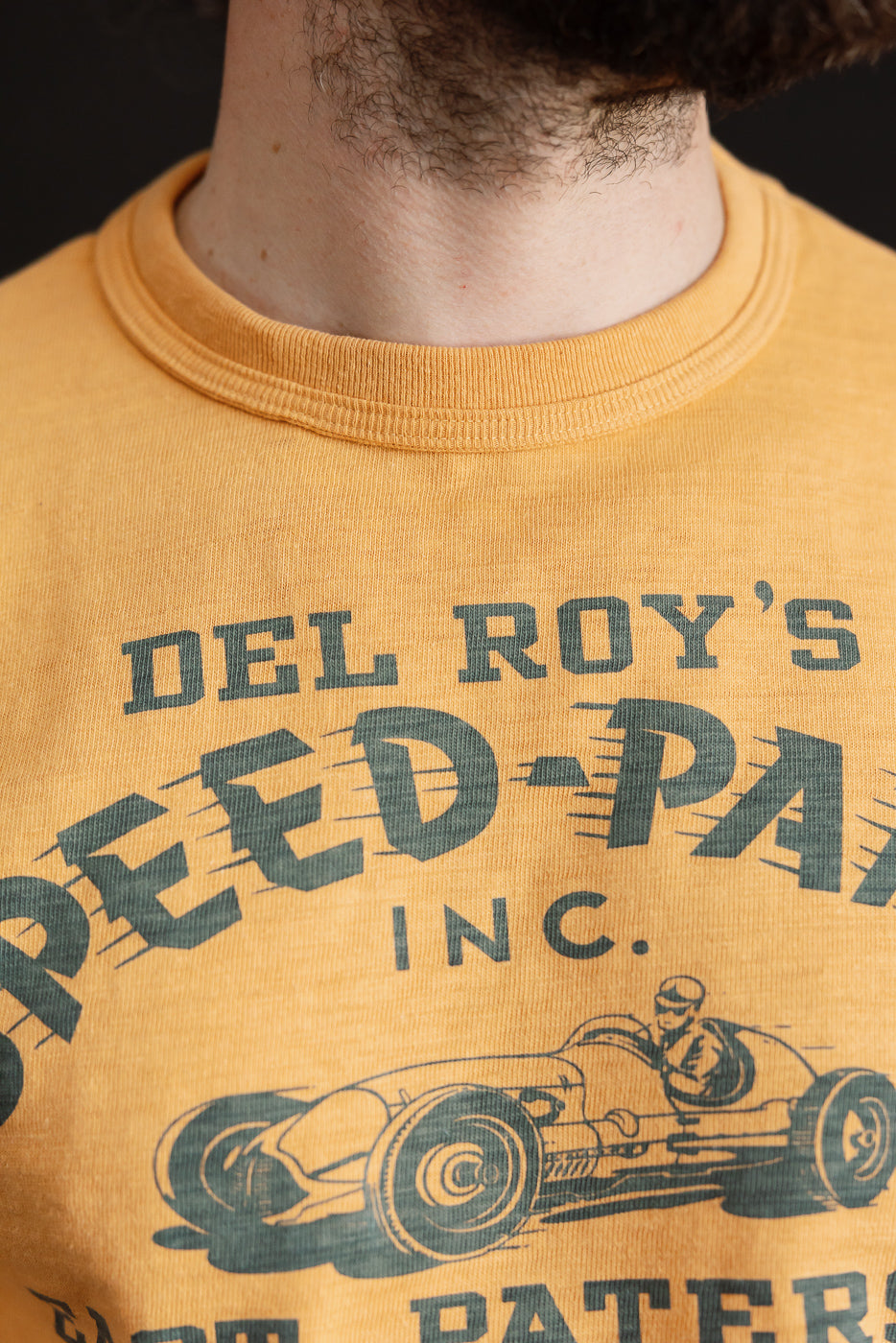 Close-up front view of Warehouse & Co. slubby cotton t-shirt in orange, showing ribbed crewneck collar and Speed Parts graphic, worn by male model 5'9