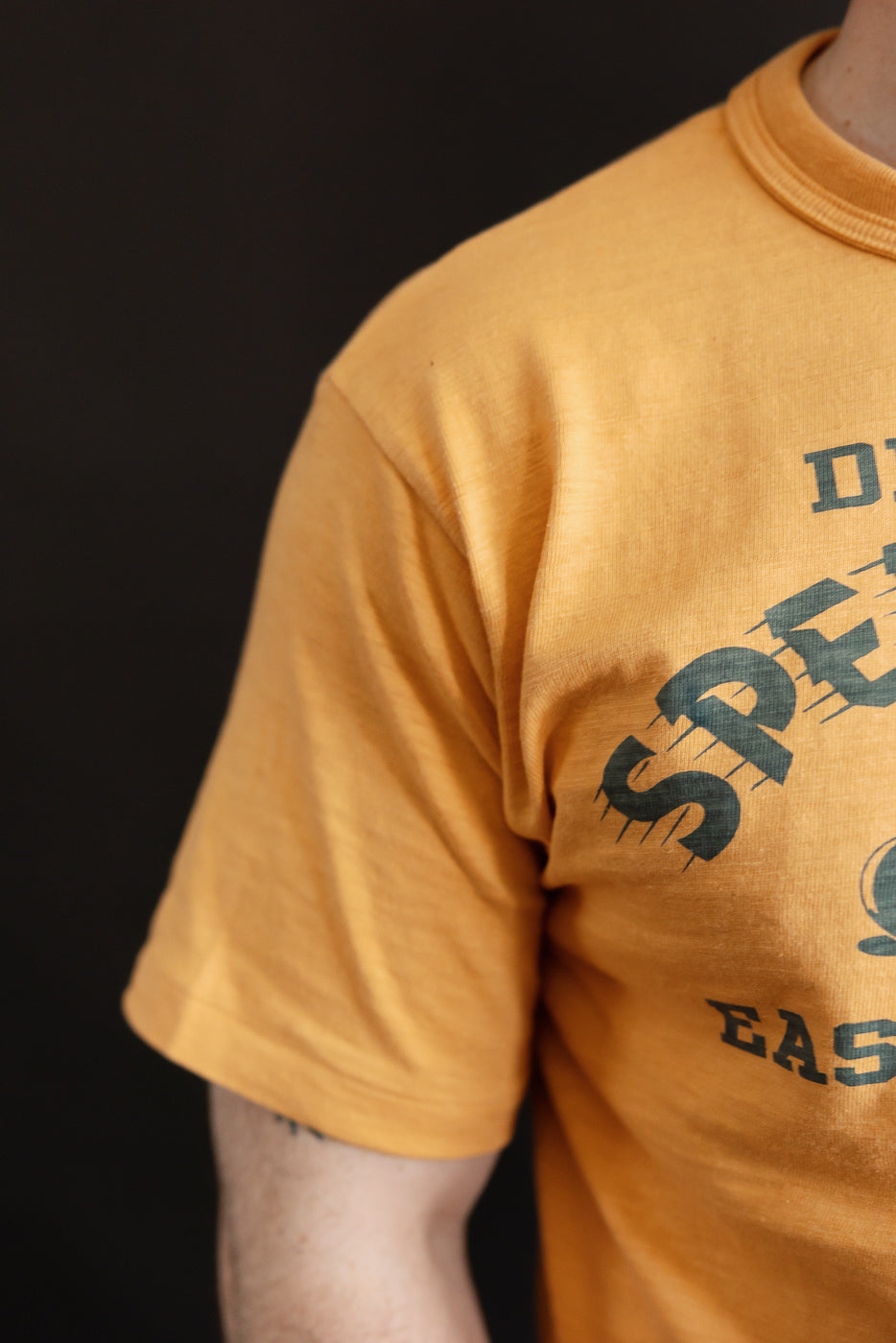 Close-up of front left chest and sleeve, orange slubby cotton t-shirt with Speed Parts graphic on male model, 5'9