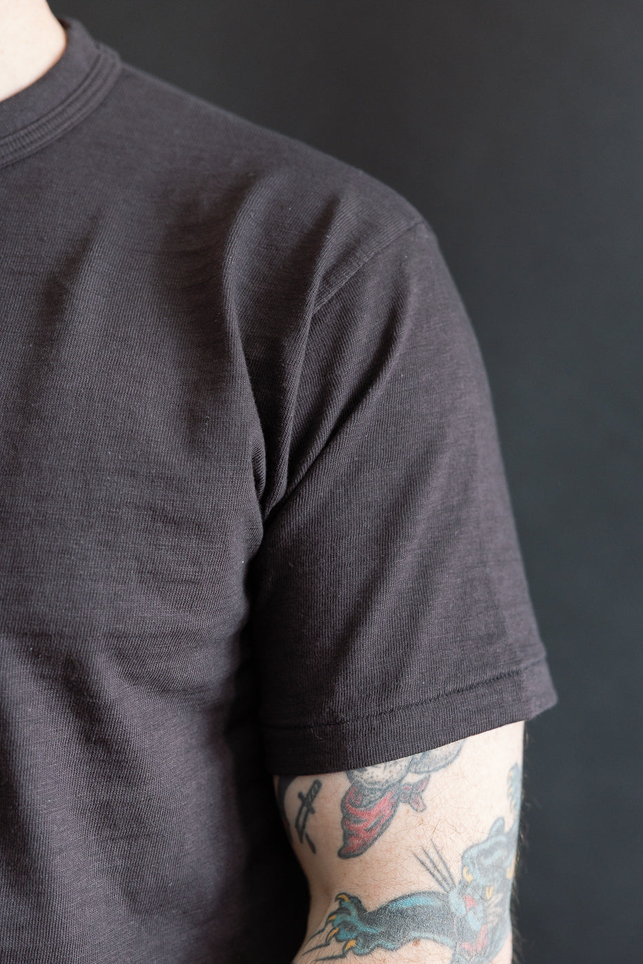Close-up of a slubby black cotton T-shirt sleeve, front view on male model, 5'9