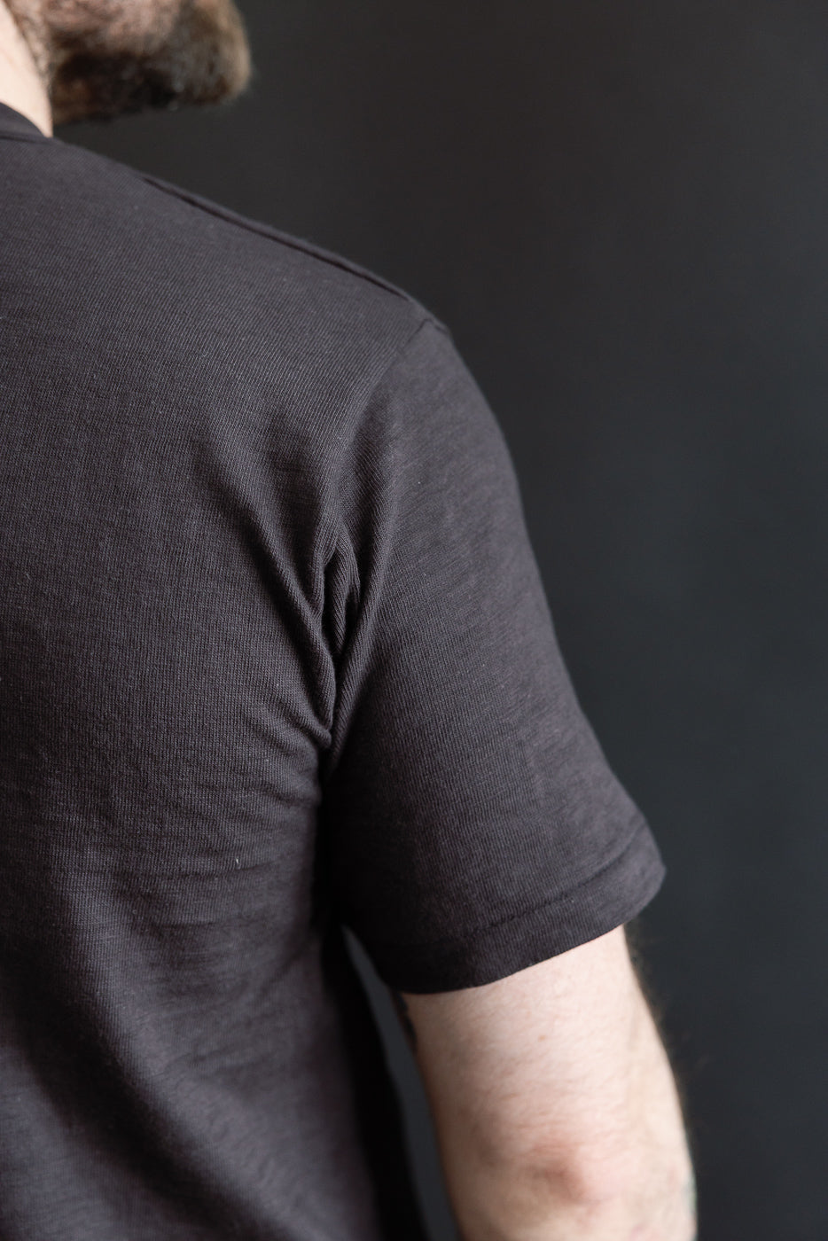 Close-up of male model's right back shoulder, athletic build, in slubby black cotton T-shirt