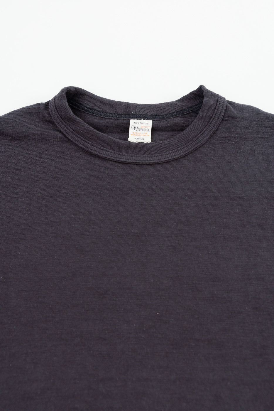 Close-up of front upper chest and collar of black slubby cotton t-shirt laying flat, showing crew neck, ribbed neckline, and inner tag details.